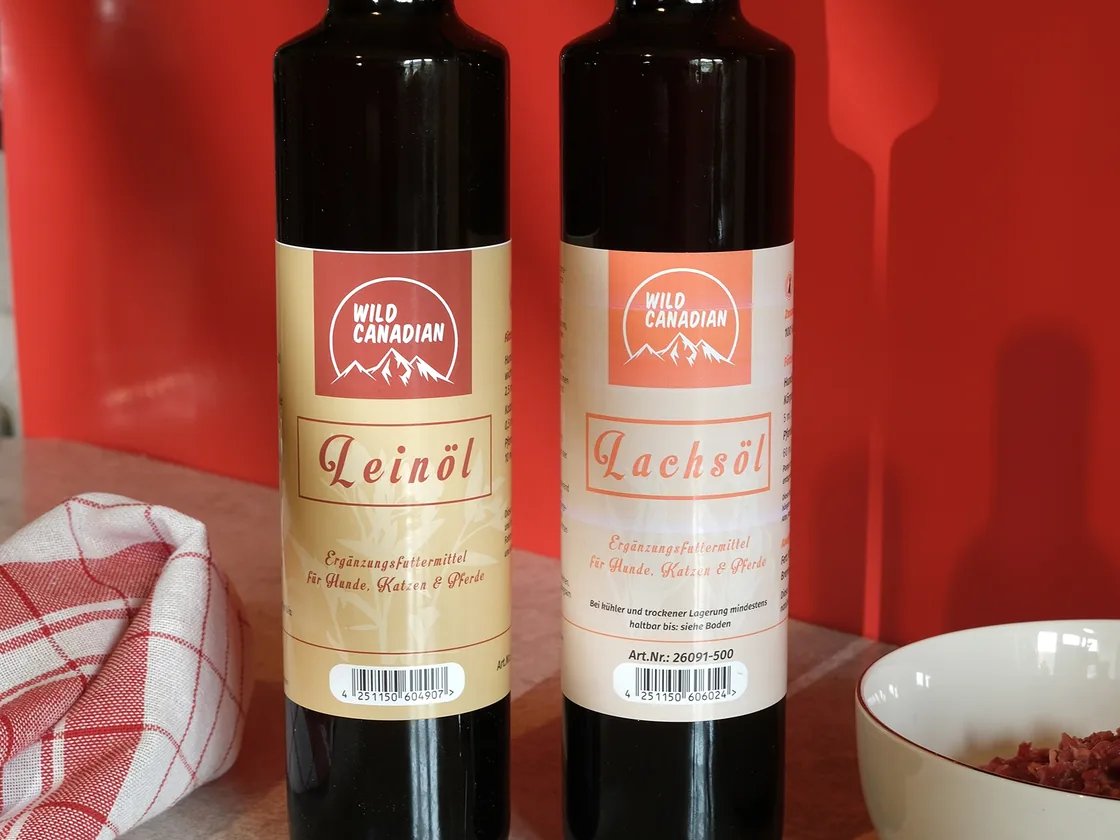 Flaschen Leinöl und Lachsöl neben einer Schüssel Frostfleisch
